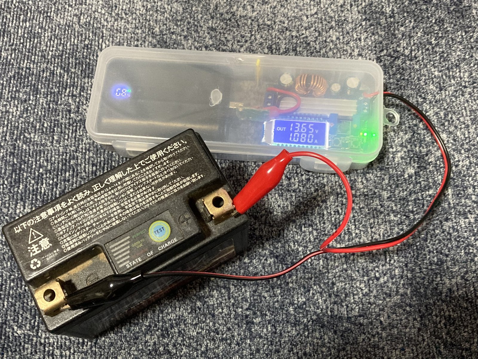 バイクのバッテリーに充電器のクリップを接続し、電圧計が13.65Vを表示している様子