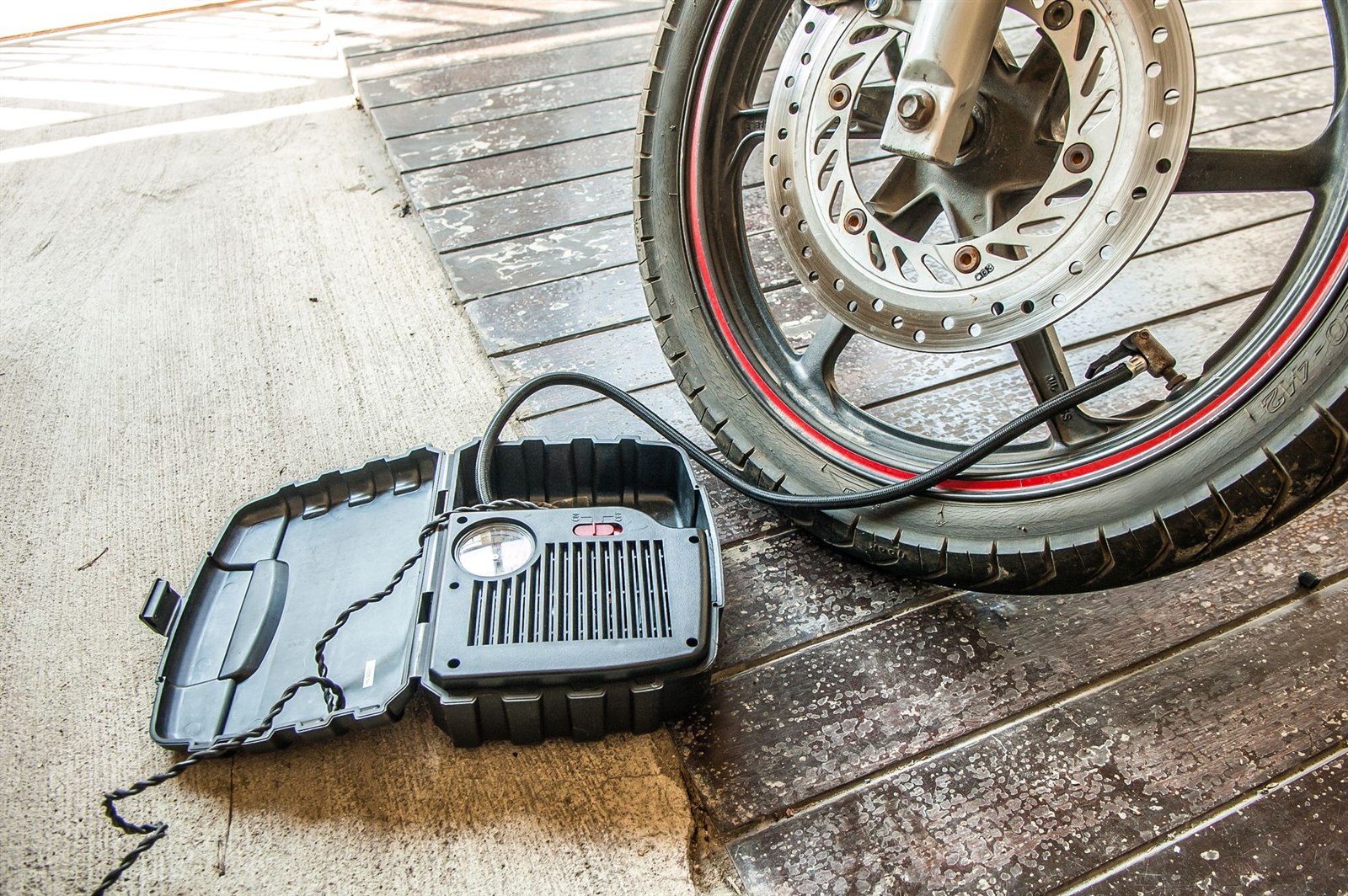 バイクの前輪のバルブにホースをつなぎ、ケースに入ったメーター付きの電動空気入れで空気を入れているところ
